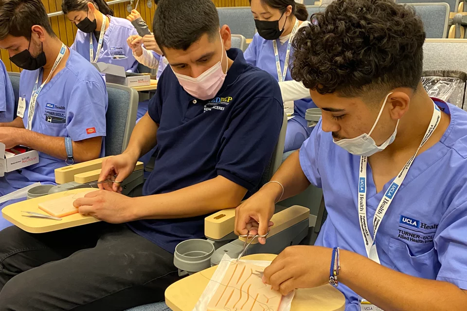 Kevin Caceres, UCLA MEDPEP Peer Mentor, teaching a high school student how to suture.