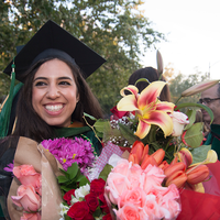 A graduating student holds a large bouquet of flowers after the commencement ceremony.