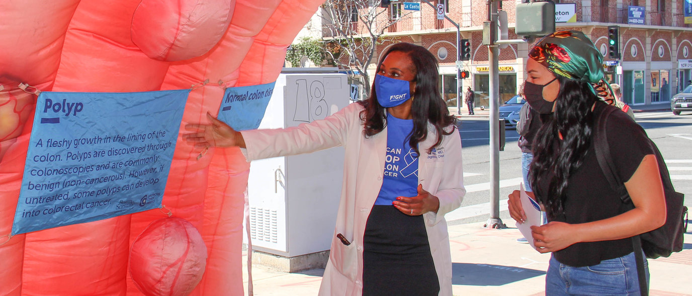 How to Prevent Cancer Via Lifestyle Choices. People look at a colon cancer awareness display