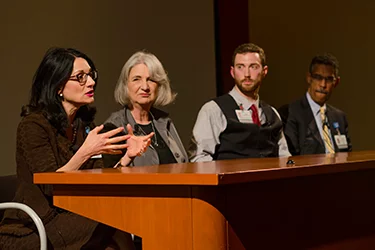 Four people at a conference desk speaking 