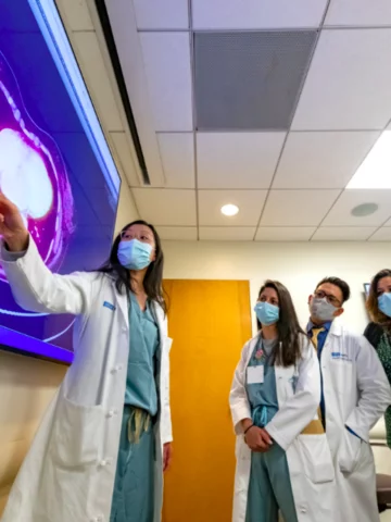 A group of masked residents and physicians reviewing results on a large digital screen