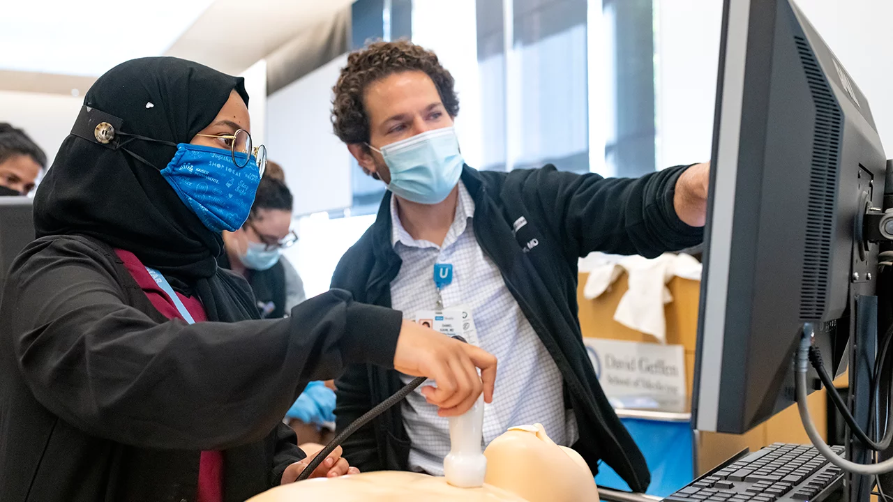 An attending guides a 4th year medical student through a hands on exercise