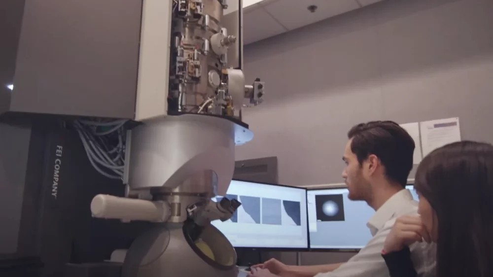 Two researchers review data on the screen of a large, powerful microscope"