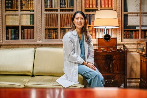 Woman resident sitting in a research room, in scrubs and a white coat