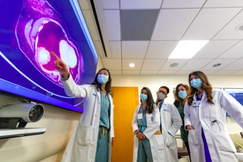 A group of masked residents and physicians reviewing results on a large digital screen