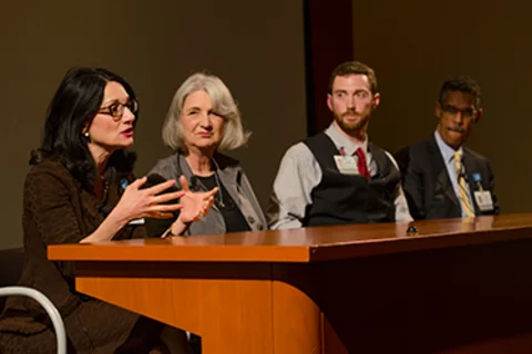 Four people at a conference desk speaking
