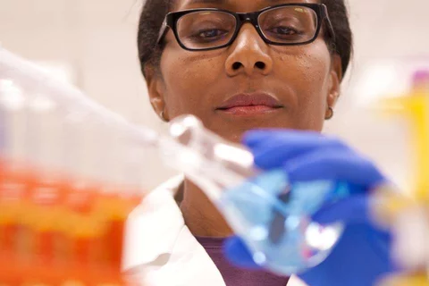 A black doctor with a beaker, piping liquid into it.